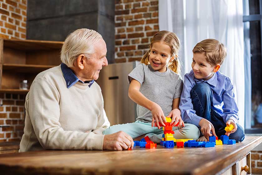 Get involved. Pleasant caring aged man gathering building blocks with his grandchildren